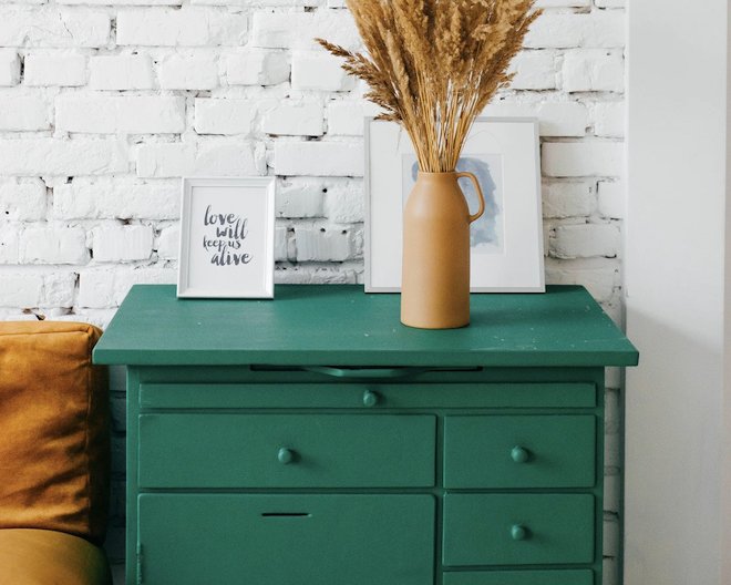 Image of a dark green drawers with vase on top of it